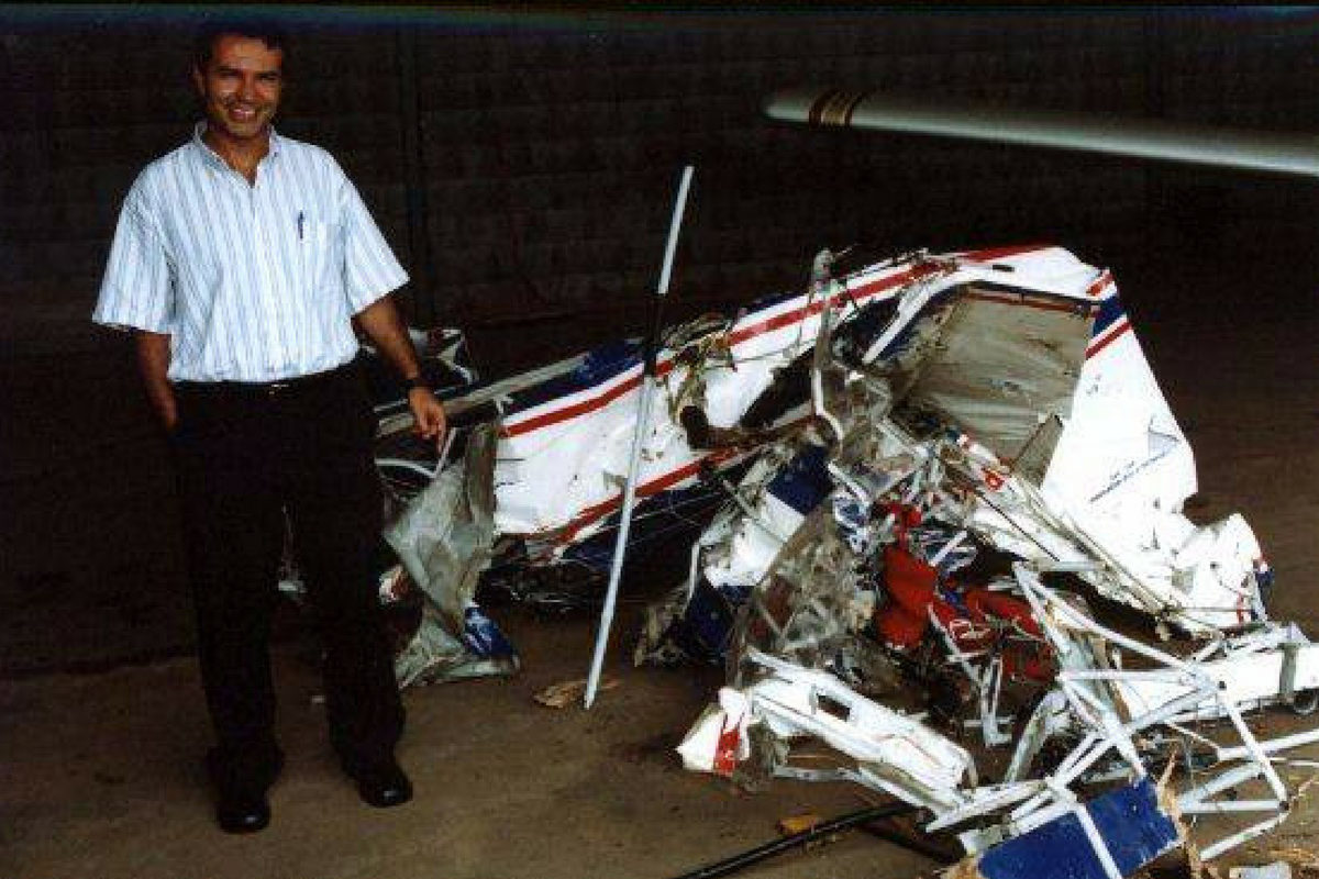 Paulo Henrique stands smiling next to a crashed airplane