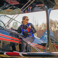 woman rests foot on vintage aircraft wearing blue back parachute