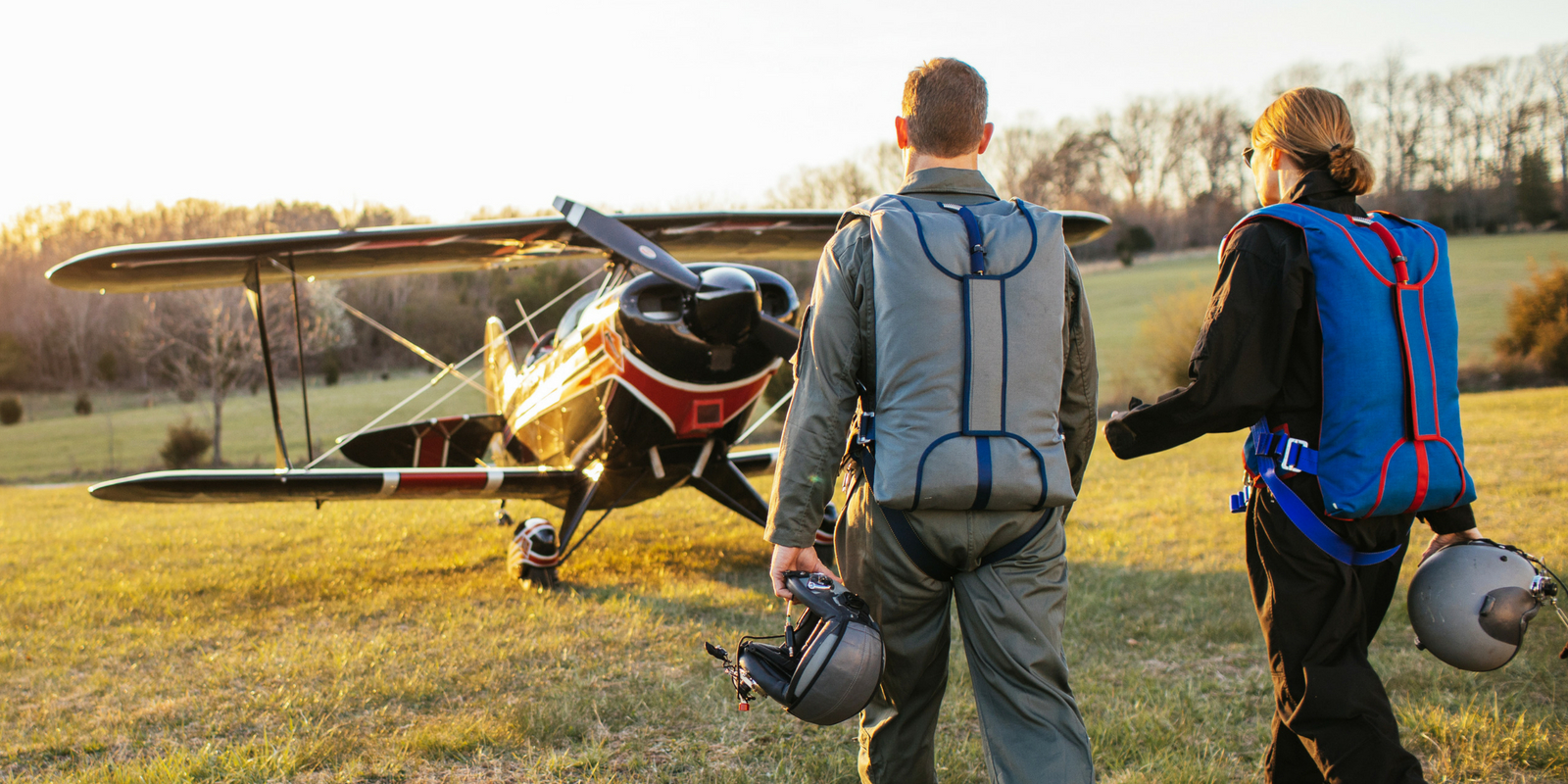 two pilots walk into the sunset wearing blue and gray Butler back parachutes